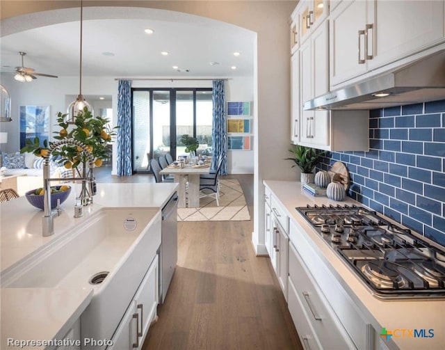 kitchen with dark wood-type flooring, white cabinets, backsplash, appliances with stainless steel finishes, and decorative light fixtures