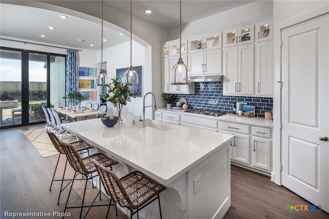 kitchen featuring white cabinetry, pendant lighting, dark wood-type flooring, stainless steel gas cooktop, and a kitchen island with sink