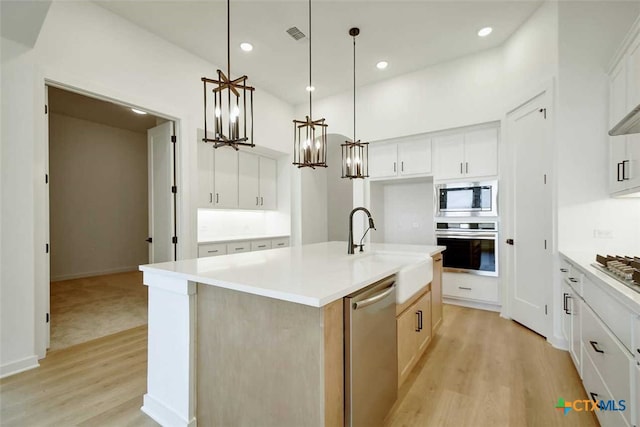 kitchen featuring white cabinetry, appliances with stainless steel finishes, an island with sink, and hanging light fixtures