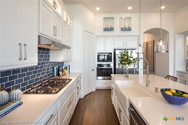 kitchen featuring sink, appliances with stainless steel finishes, hanging light fixtures, white cabinets, and dark wood-type flooring