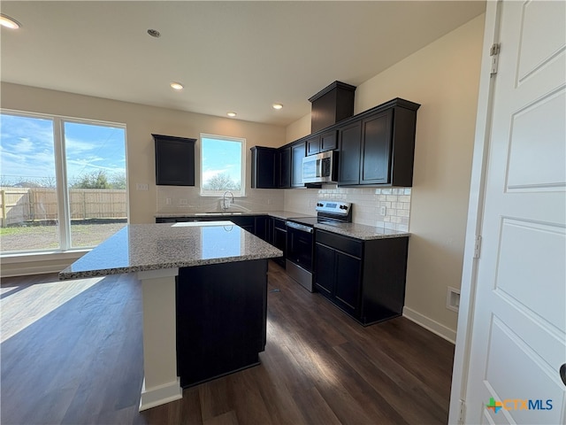 kitchen featuring appliances with stainless steel finishes, tasteful backsplash, dark hardwood / wood-style flooring, a center island, and light stone countertops