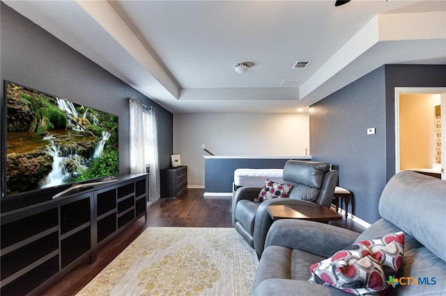 living area with a raised ceiling, wood finished floors, visible vents, and baseboards