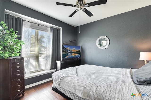 bedroom featuring wood finished floors, baseboards, a textured wall, and ceiling fan