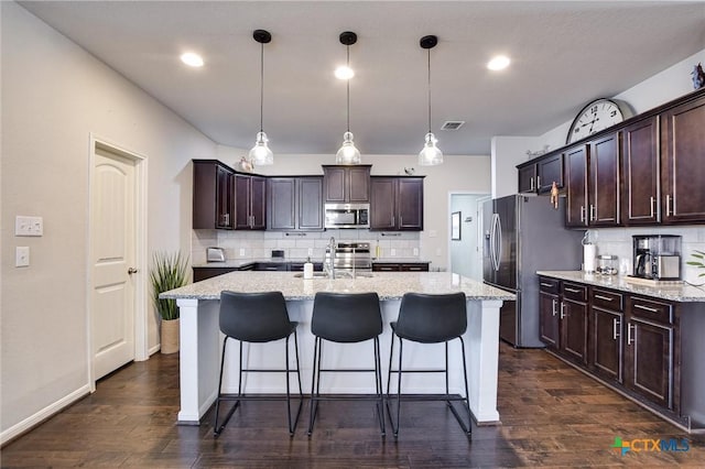 kitchen featuring dark wood-type flooring, dark brown cabinetry, a breakfast bar, stainless steel appliances, and a kitchen island with sink