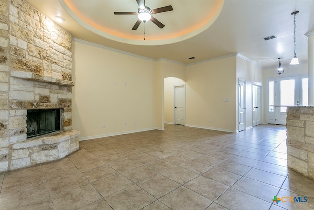 unfurnished living room with light tile patterned floors, ceiling fan, crown molding, a raised ceiling, and a fireplace