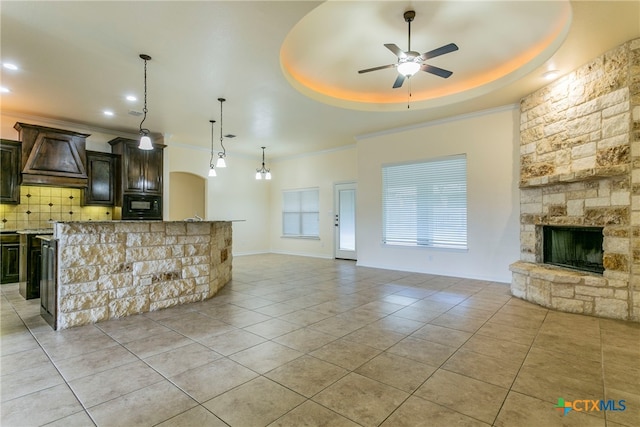 unfurnished living room featuring a fireplace, light tile patterned floors, ceiling fan, and a tray ceiling