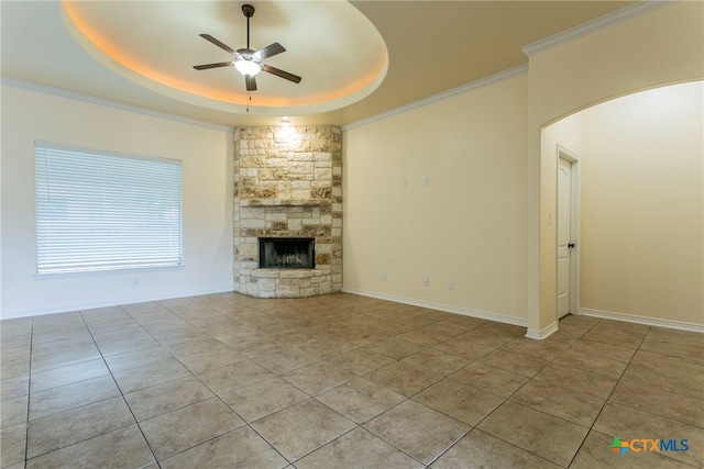 unfurnished living room featuring ornamental molding, a stone fireplace, light tile patterned floors, a tray ceiling, and ceiling fan