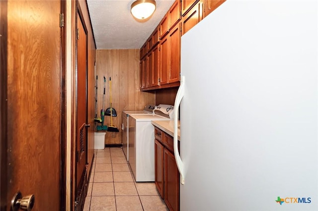 clothes washing area with wooden walls, light tile patterned floors, washer and dryer, cabinet space, and a textured ceiling