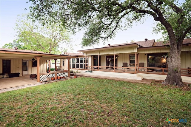 back of property featuring board and batten siding, a lawn, a patio area, and a deck