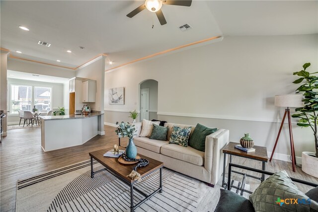 living room featuring lofted ceiling, ceiling fan, wood-type flooring, and crown molding