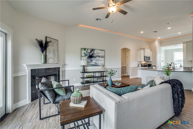 living room with ceiling fan, light wood-type flooring, crown molding, and a tiled fireplace