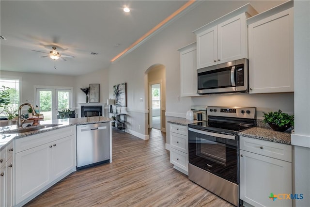 166 Lost Maples Way, Marion, TX 78124 - kitchen with stainless steel appliances, arched walkways, a sink, light stone countertops, and a fireplace