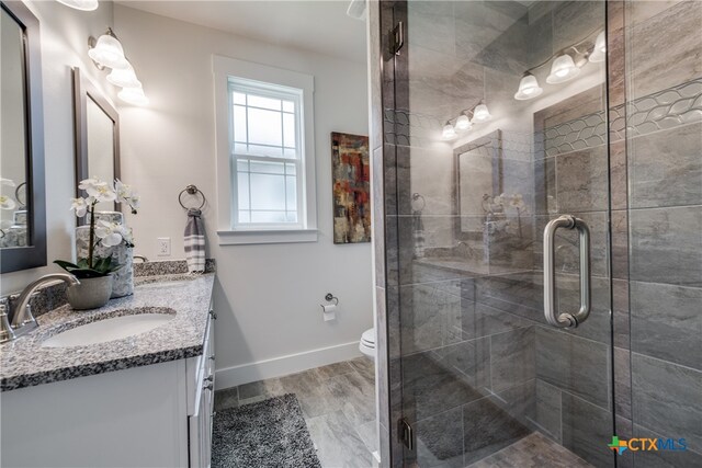 bathroom with an enclosed shower, vanity, toilet, and wood-type flooring