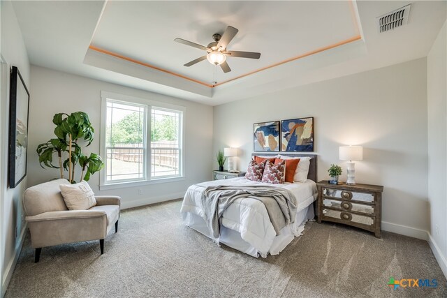 carpeted bedroom featuring a raised ceiling and ceiling fan