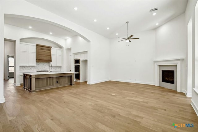 unfurnished living room featuring ceiling fan, sink, light hardwood / wood-style floors, and a high ceiling