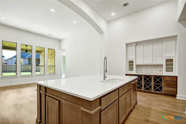 kitchen with tasteful backsplash, light hardwood / wood-style flooring, a center island with sink, and sink