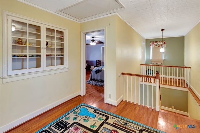 hallway with an upstairs landing, ornamental molding, attic access, and wood finished floors