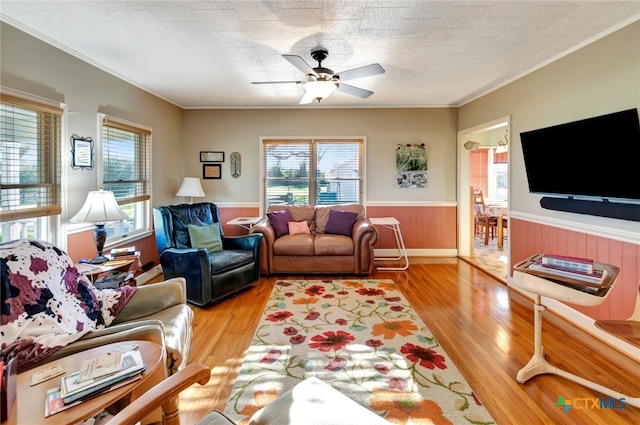 living room with a wainscoted wall, a healthy amount of sunlight, light wood-style flooring, and crown molding