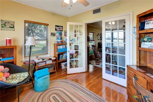 living area featuring a wealth of natural light, ornamental molding, a ceiling fan, wood finished floors, and french doors