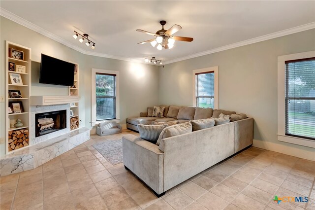 tiled living room featuring rail lighting, ceiling fan, crown molding, built in features, and a high end fireplace