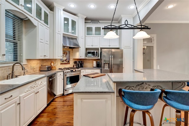 kitchen featuring appliances with stainless steel finishes, decorative light fixtures, exhaust hood, sink, and a center island