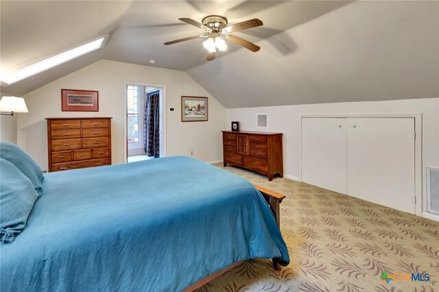 carpeted bedroom with a closet, vaulted ceiling with skylight, ceiling fan, and ensuite bathroom