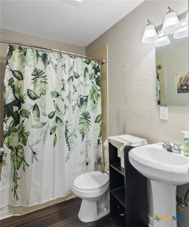 full bath with a textured wall, toilet, wood finished floors, and a shower with shower curtain