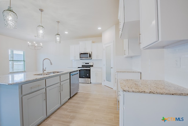 kitchen featuring stainless steel appliances, a center island with sink, pendant lighting, sink, and white cabinetry