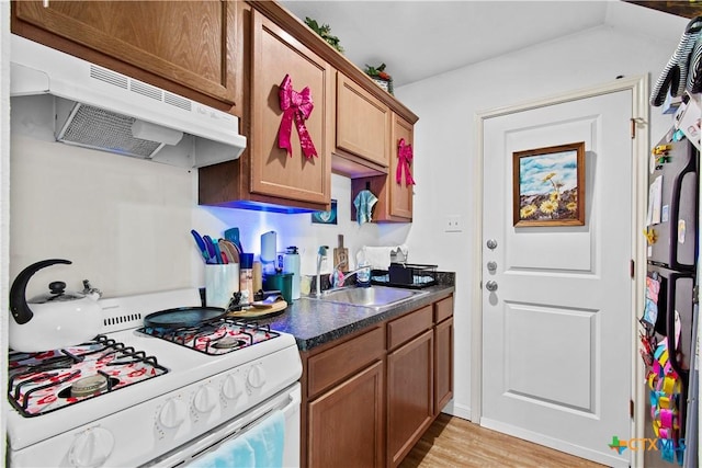 kitchen featuring brown cabinets, dark countertops, a sink, gas range gas stove, and under cabinet range hood