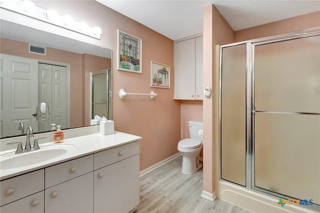 bathroom featuring visible vents, toilet, vanity, a shower stall, and wood finished floors