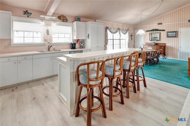 kitchen featuring vaulted ceiling with beams, light wood-style floors, a sink, and a healthy amount of sunlight