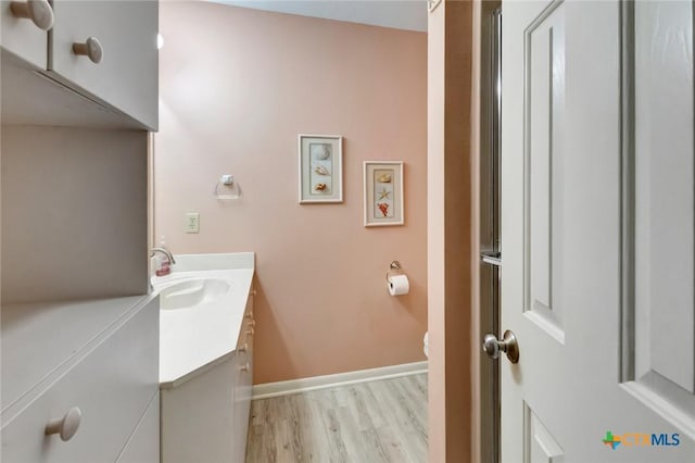 bathroom featuring toilet, baseboards, wood finished floors, and vanity