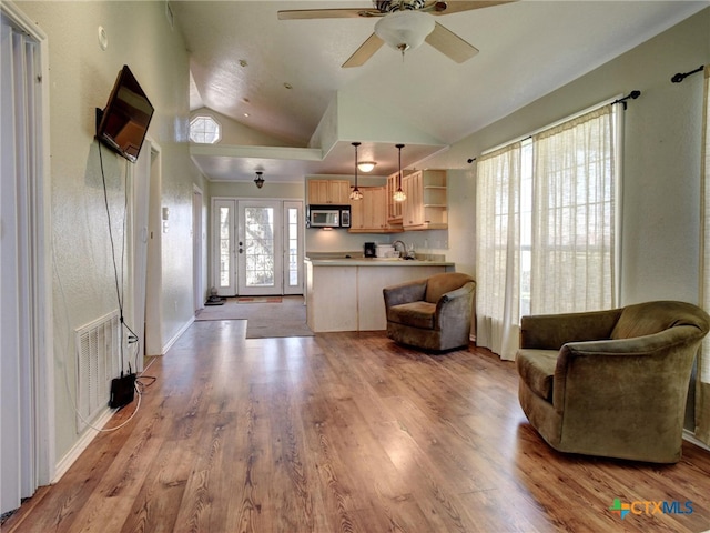 living area featuring lofted ceiling, light wood-style floors, ceiling fan, and visible vents