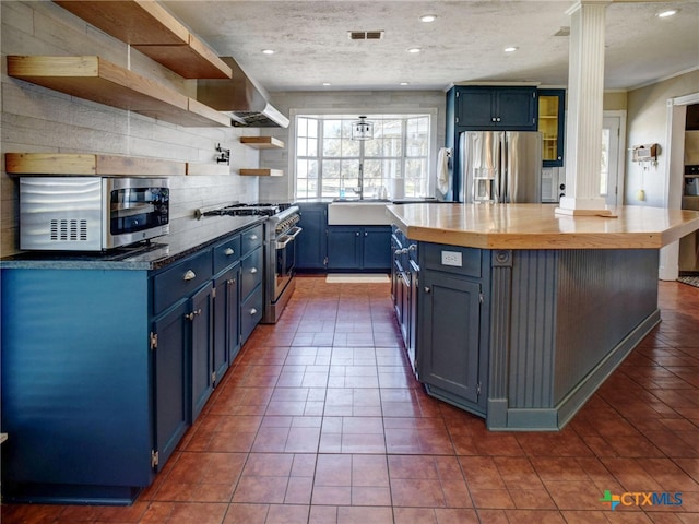 kitchen with a kitchen island, appliances with stainless steel finishes, blue cabinets, ornate columns, and open shelves