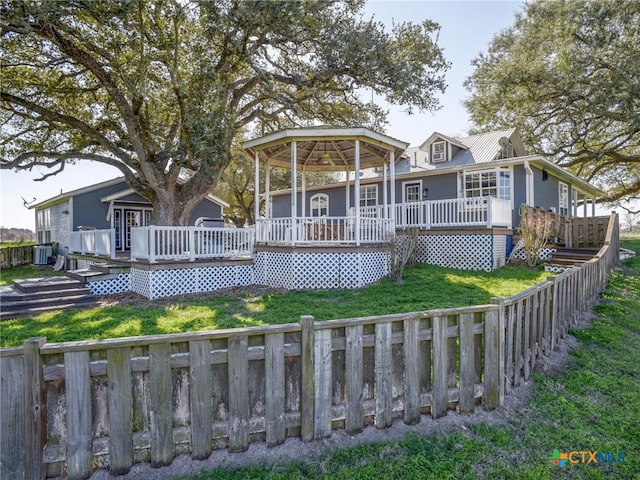 view of front facade with metal roof, fence private yard, a deck, central air condition unit, and a front yard