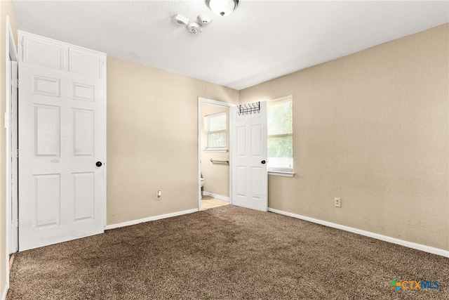 unfurnished bedroom featuring ensuite bath, carpet flooring, and baseboards