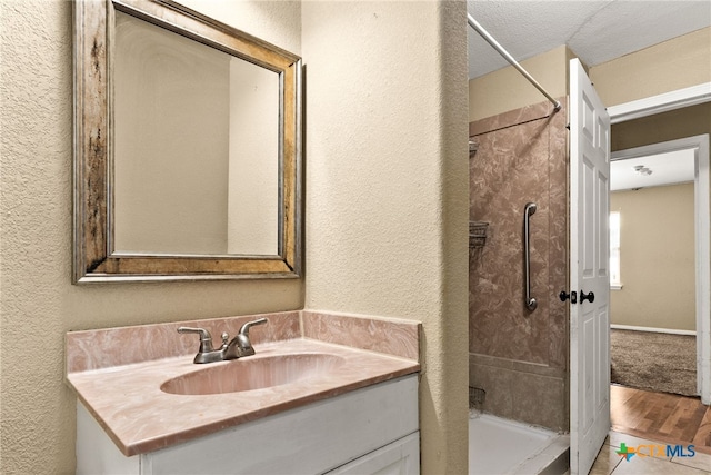 bathroom featuring a shower, a textured wall, and vanity