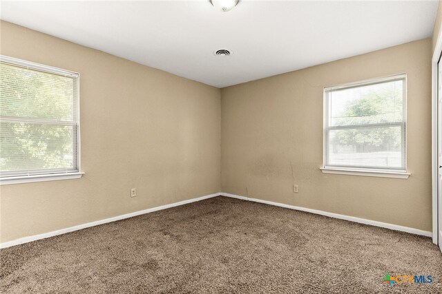 unfurnished room with a wealth of natural light, carpet flooring, and visible vents