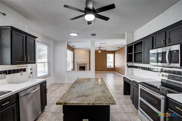 kitchen featuring tasteful backsplash, stainless steel appliances, light tile patterned floors, a kitchen island, and a tiled fireplace