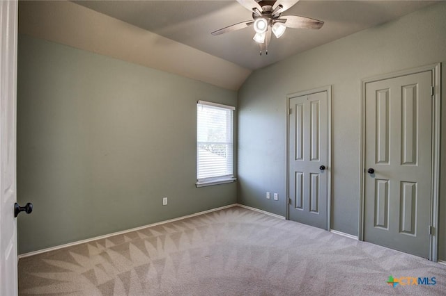 unfurnished bedroom featuring carpet flooring, two closets, vaulted ceiling, and ceiling fan