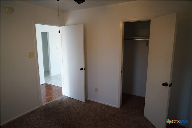 unfurnished bedroom featuring dark colored carpet, a closet, and ceiling fan