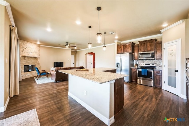 kitchen featuring dark brown cabinetry, decorative backsplash, appliances with stainless steel finishes, a fireplace, and arched walkways