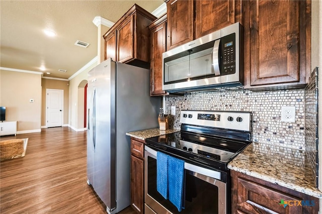 kitchen with wood finished floors, visible vents, arched walkways, ornamental molding, and appliances with stainless steel finishes