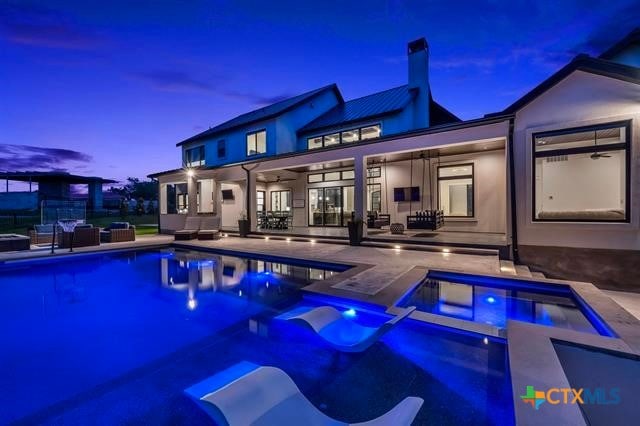 pool at dusk with an outdoor living space, a patio area, ceiling fan, and an in ground hot tub