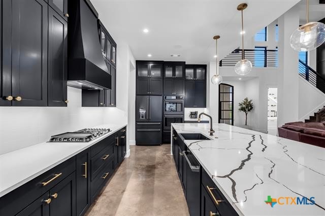 kitchen featuring stainless steel appliances, sink, custom range hood, light stone countertops, and pendant lighting