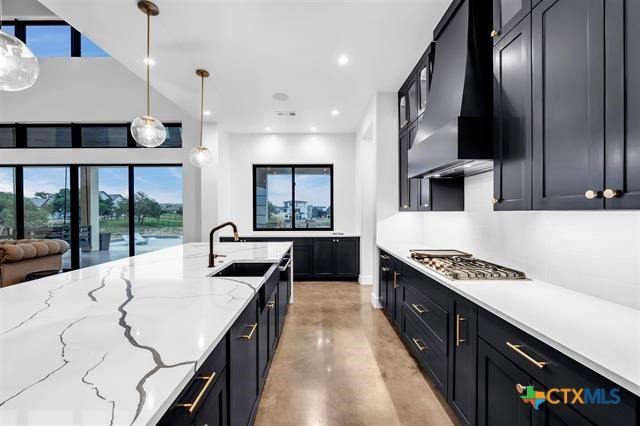 117 Legendary Estates Dr, Burnet, TX 78611 - kitchen with ventilation hood, concrete floors, stainless steel gas stovetop, dark cabinets, and a sink