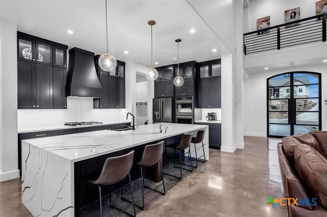 kitchen with stainless steel appliances, hanging light fixtures, sink, custom exhaust hood, and a large island with sink