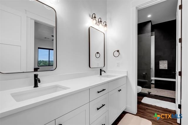 bathroom featuring hardwood / wood-style flooring, vanity, toilet, and a tile shower