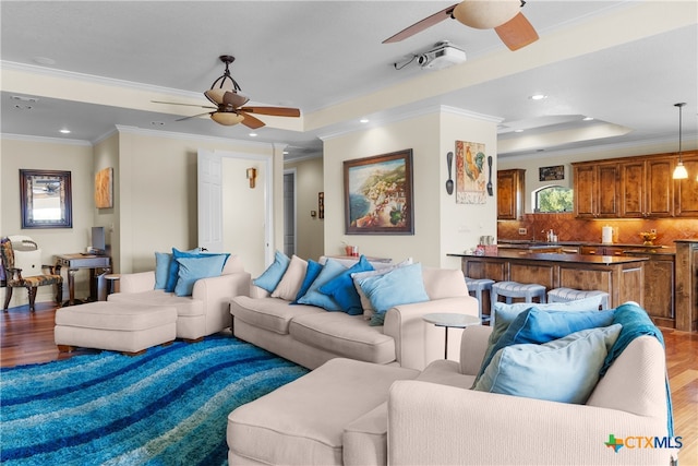 living room with light hardwood / wood-style floors, ceiling fan, a tray ceiling, and ornamental molding