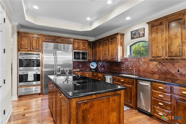 kitchen with light hardwood / wood-style floors, a center island with sink, built in appliances, tasteful backsplash, and ornamental molding